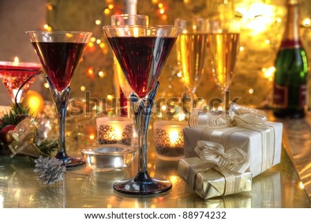 Red wine in glasses,champagne, gift boxes, candle lights on golden background with twinkle lights.