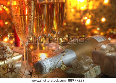 Closeup of champagne in glasses,bottle,gift boxes,candle lights  and twinkle lights on golden background.