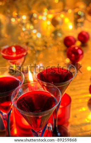 Closeup of red wine in glasses, candle light, baubles on blurred background with twinkle lights.