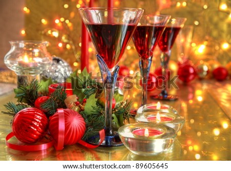 Red wine in glasses,baubles,candle lights,green twig and twinkle lights on golden background.