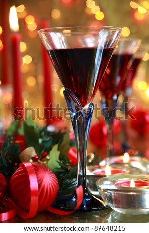 Closeup of glasses with wine, baubles,green twig,candle lights on background with twinkle lights.