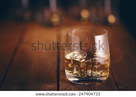 Glass of whiskey on a wooden table bar on the background of bright lights of the bar