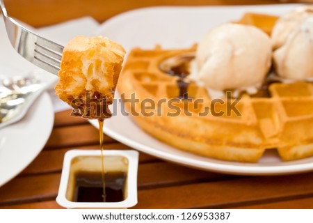 Delicious waffle on fork with syrup and  top icecream in the background