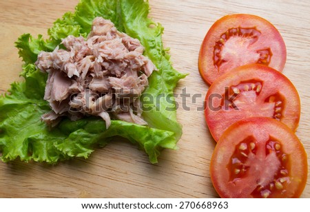Canned tuna meat with tomato and lettuce on wood background