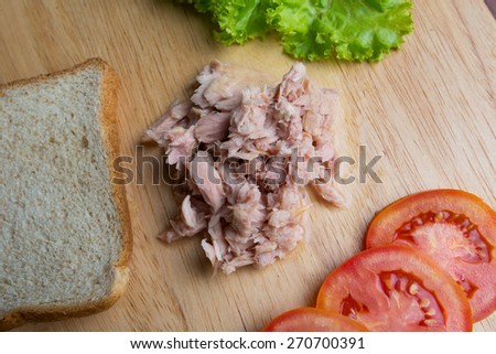 Canned tuna meat prepared for sandwich with bread, lettuce and tomato on wood background