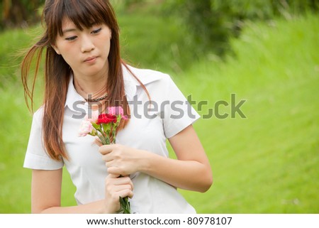 Beautiful young Thai girl holding pink carnation flower and thinking of someone