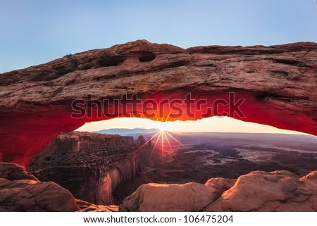 The sun rises within Mesa arch in Canyonlands National Park, Utah causing the red rock to glow and illuminate.