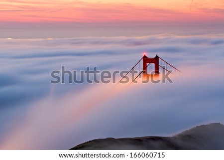 The Northern tower of the Golden Gate Bridge as almost all of the bay is shrouded in fog during sunrise.