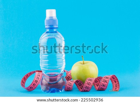 bottle of water, measuring tape and apples on blue background