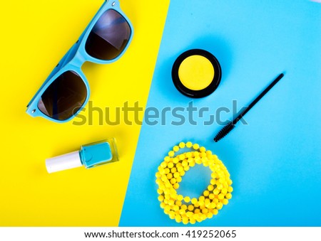 Summer accessories and cosmetics for relaxation on a yellow background - sunglasses, lipstick, powder, colored beads, nail polish. View from above. Flat lay.