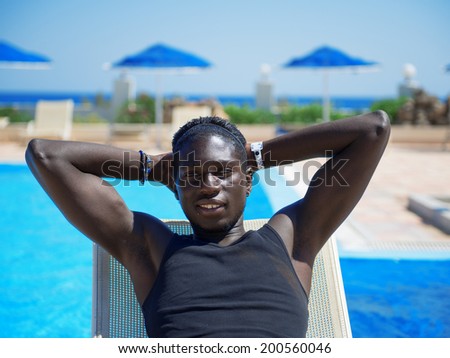 Young African American Man Sitting by the Pool Relaxing in the Hotel on the Beach. Looking at camera.