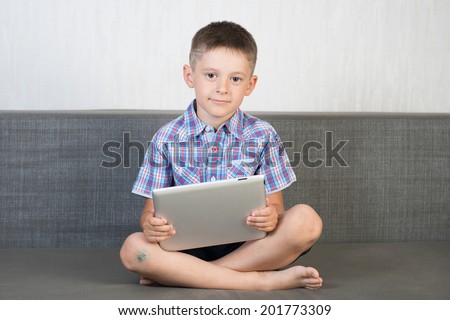 Smiling boy indoor. Sitting on the sofa with tablet with tablet