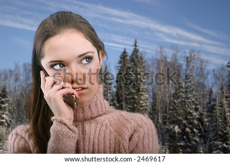 portrait of beauty teen girl call by cell phone on winter forest background