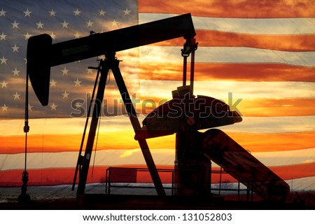 Landscape image of a oil well pumpjack wiith an early morning golden sunrise and American USA red White and Blue Flag background.