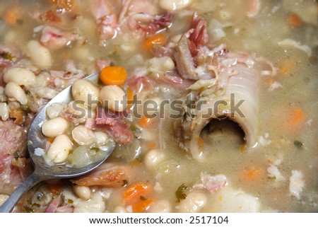 Spoon in a Navy bean soup with ham,bone onion celery and carrots.