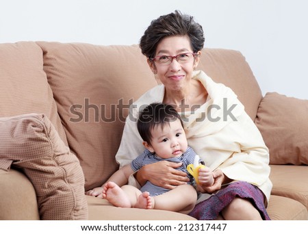 Old woman holding Thai baby smiling and sitting on the sofa