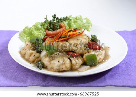 Fish fried with Thai herbs and black pepper, the image isolated on dish and fabric background