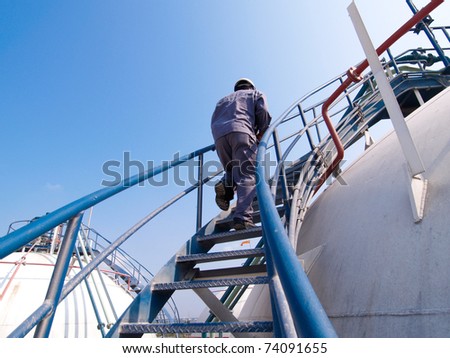 The engineer walking along the ladder of the refinery tank for checking valves and safety systems