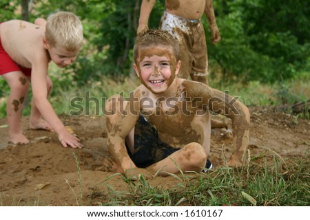 Boy painted with mud sitting in dirt hole with other boys playing in background
