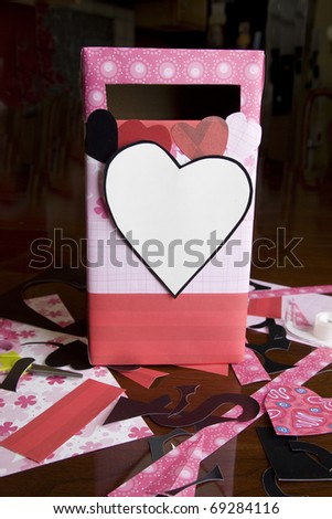 A child\'s handmade Valentine exchange box with paper and crafting supplies scattered on table.