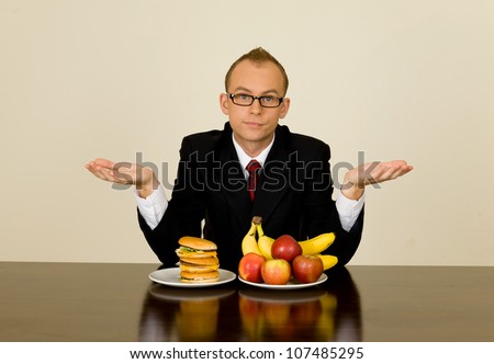 Young businessman during his lunch time trying to make a choice to eat healthy or junk food