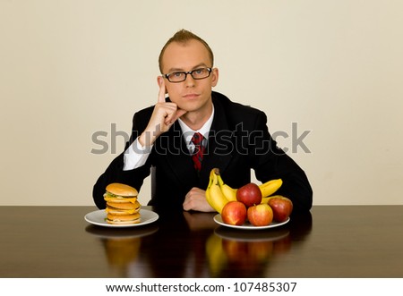Young businessman during his lunch time trying to make a choice to eat healthy or junk food