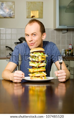 Happy young man is going to eat big layered cheeseburger