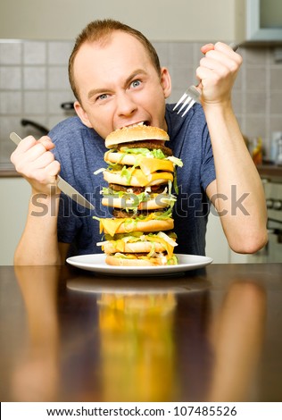 Happy young man is going to eat big layered cheeseburger