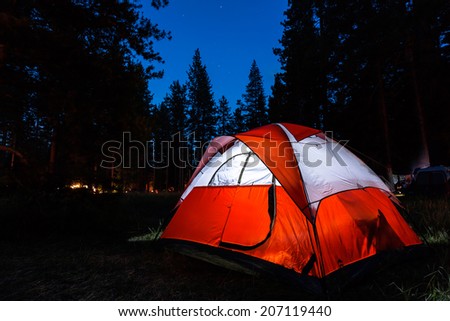 Campsite with illuminated tent and stars in dark sky