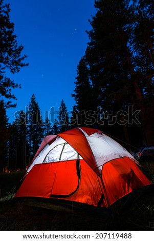Campsite with illuminated tent and stars in dark sky