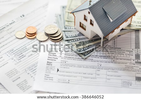 Miniature house with money on tax papers.