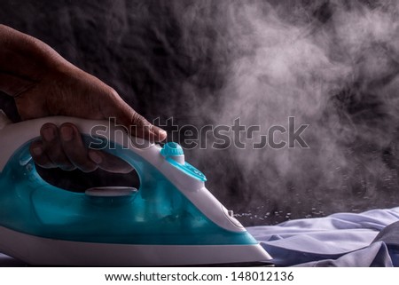 A person ironing a shirt with a steaming hot electric iron