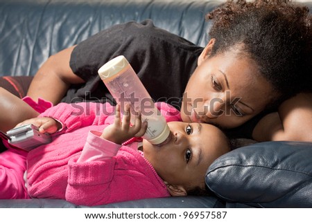 A mother and her baby girl who is drinking her bottle of milk