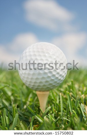 Golf Ball on Tee in front of blue sky and clouds. Vertical format.