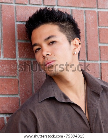 A photograph of a young man leaned against a brick wall.