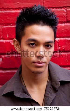 A photograph of a young man leaned against a brick wall.