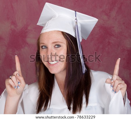 A cute girl poses for her graduation photo.  There is a pink background.