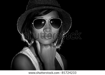 A black and white image of a beautiful model wearing sunglasses and hat.  Image is black and white.