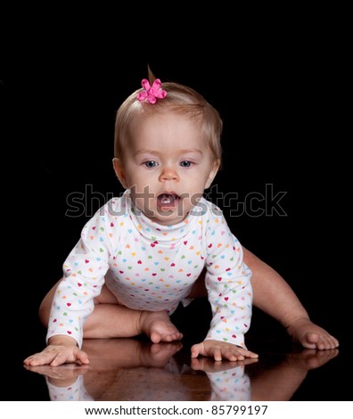 A cute image of a beautiful baby girl with a pink flower bow in her hair.  Image is isolated on black with reflection.