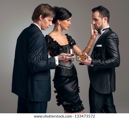 Two stylish men in suits and a girl in an evening black dress
