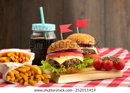 Tasty burgers with flags, french fries and beverage on wooden board