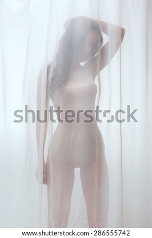 Sexy  lady with perfect fit body in combidress   behind tulle curtain