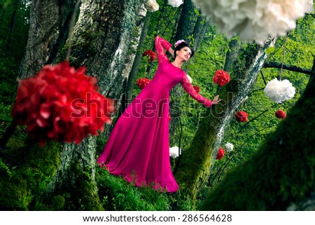 Young beautiful woman in long pink dress in the forest with decorative flowers