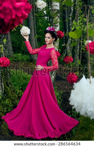 Young beautiful woman in long pink dress in the forest with decorative flowers
