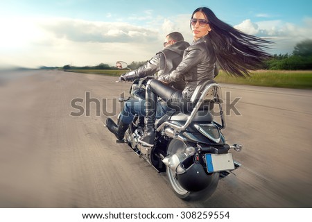 Biker Man and woman wearing black leather jackets and stylish sunglasses riding on motorcycle