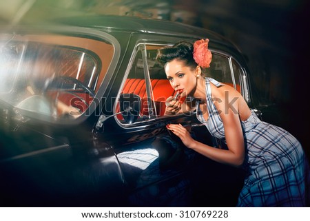 Beautiful elegant woman put lipstick on her lips near car mirror