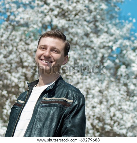 A  half-length portrait of young smiling man and a blooming tree behind him