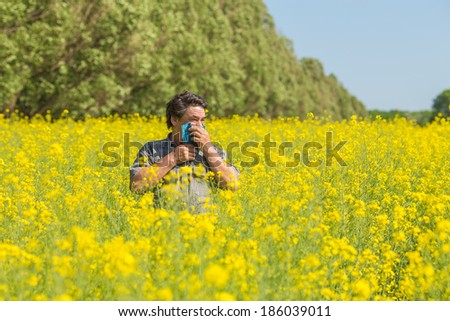 man in field blowing his nose and suffering from hay fever.