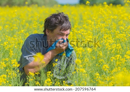 man in field blowing his nose and suffering from hay fever.