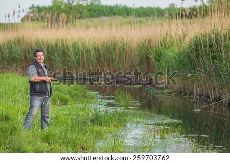 Fisherman on the river bank. Man fisherman catches a fish. Fisherman in his hand holding spinning. Fishing, spinning reel, fish. The concept of a rural getaway. Article about fishing.
